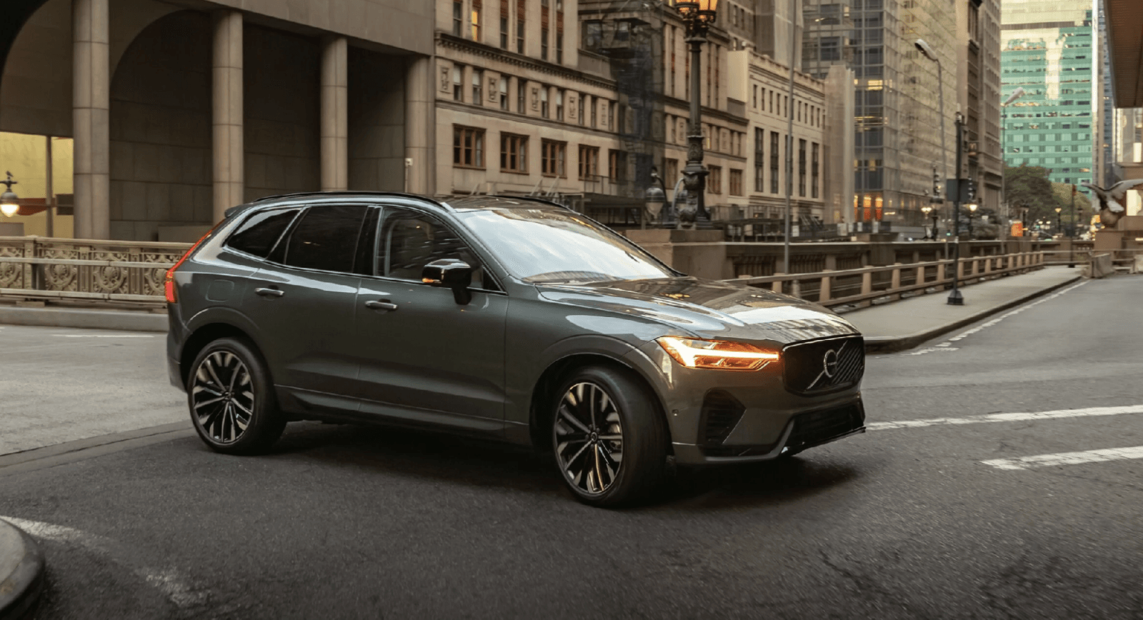 Gray Volvo XC60 SUV driving through a city street lined with historic stone buildings and street lamps