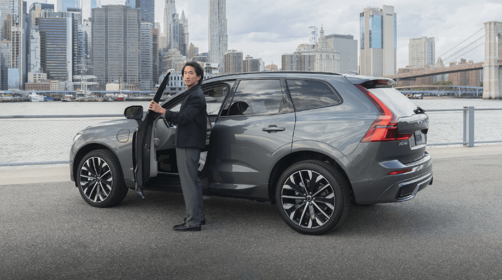 Man opening the door of a gray Volvo XC60 SUV parked along the waterfront with the New York City skyline