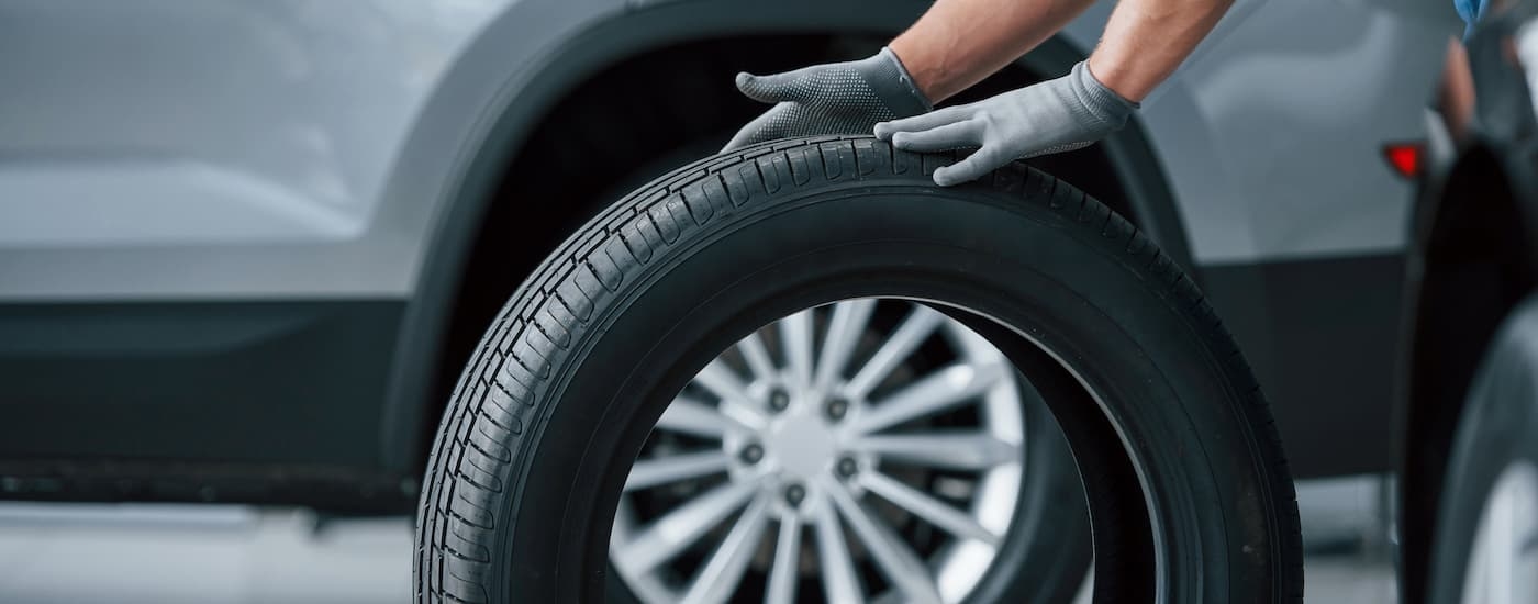 A close up of a tire being rolled near a vehicle.