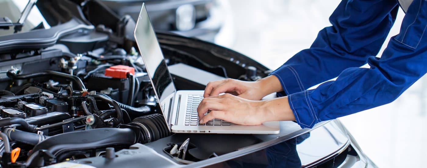 A service technician with a computer looking over the engine compartment.