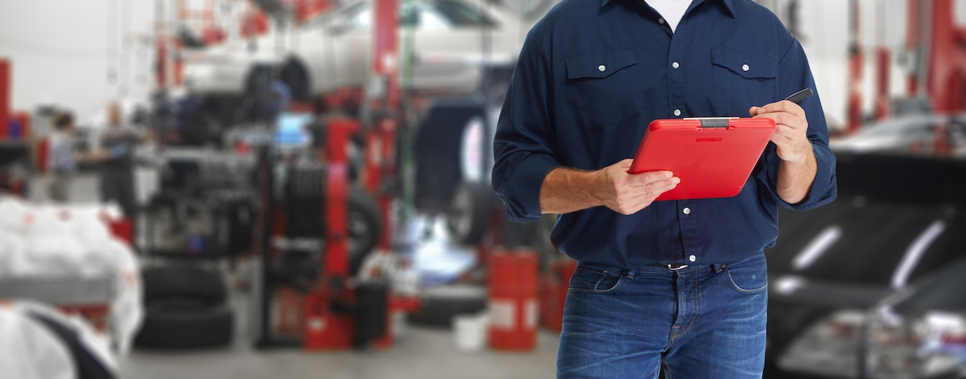 A service technician holding a clipboard in front of a vehicle.