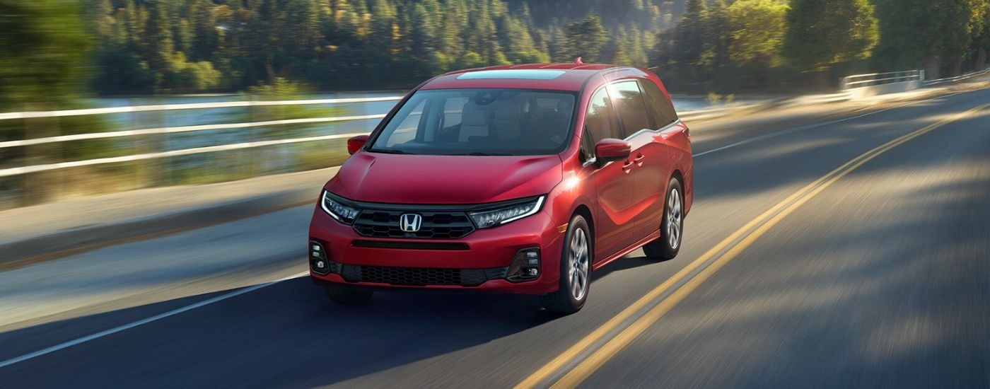 A red 2027 Honda Odyssey Elite driving by a lake.