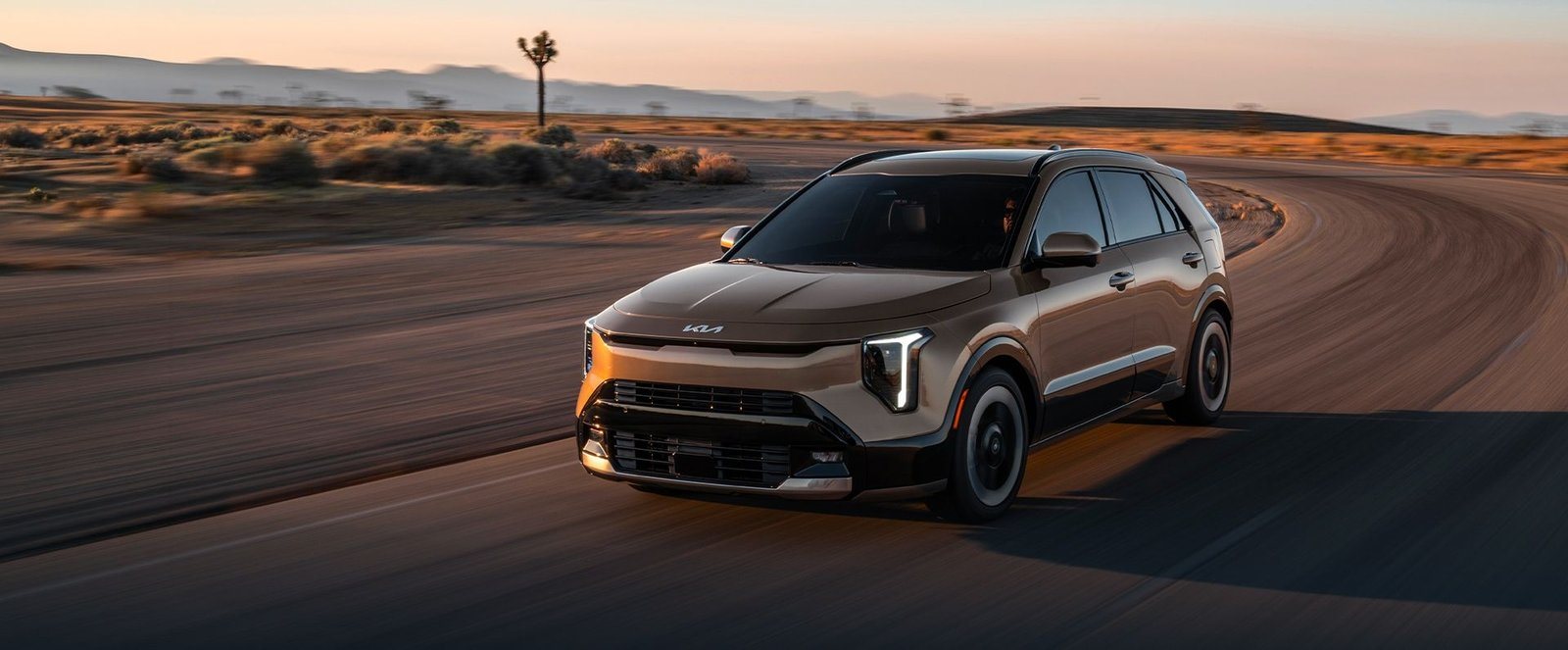 2027 Kia Niro Hybrid in bronze driving on a desert road at sunset