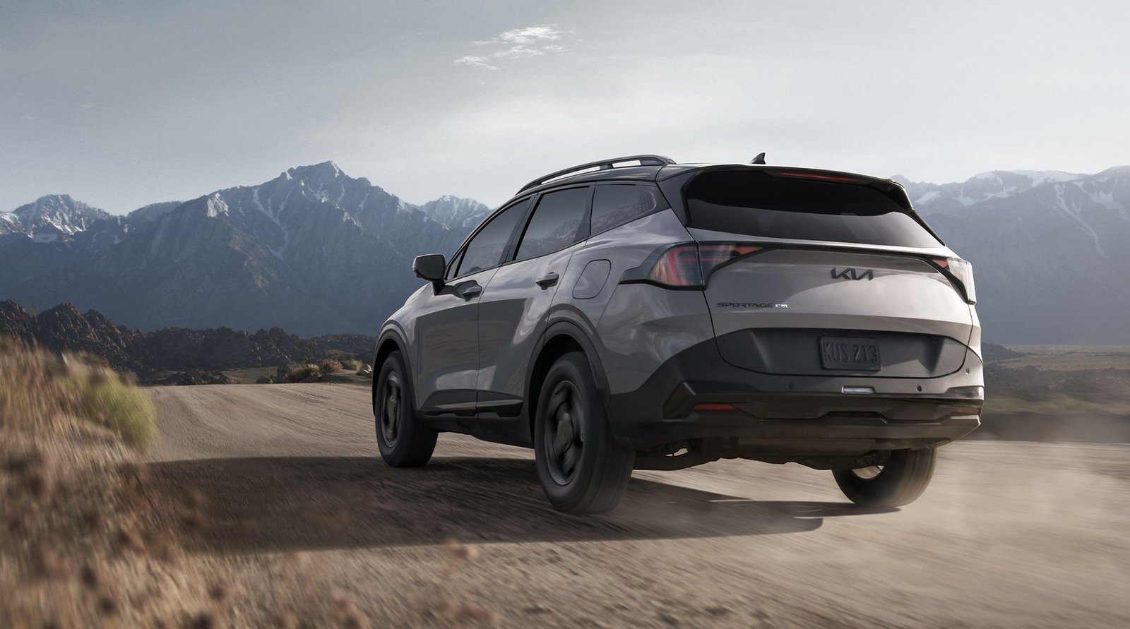 2027 Kia Sportage X-Pro driving on a dirt road below snowy mountains