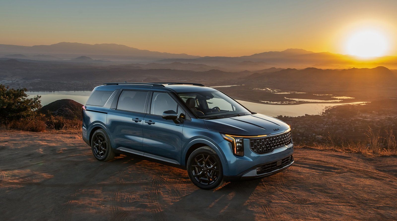 2027 Kia Carnival in blue parked on an overlook at sunset