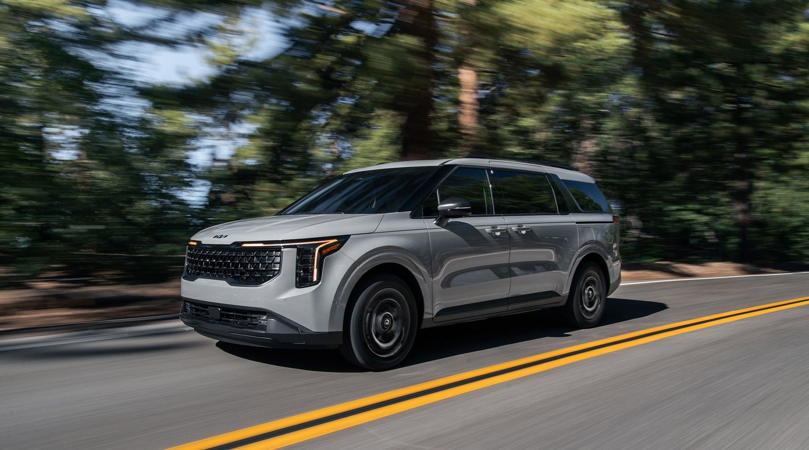 2027 Kia Carnival Hybrid in silver driving on a forest road