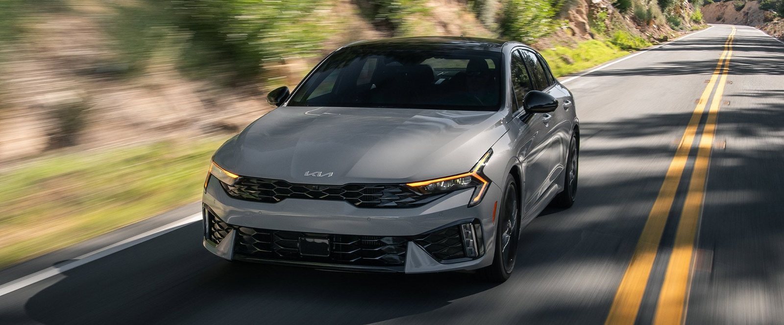 2027 Kia K5 GT-Line in gray driving on a winding mountain road