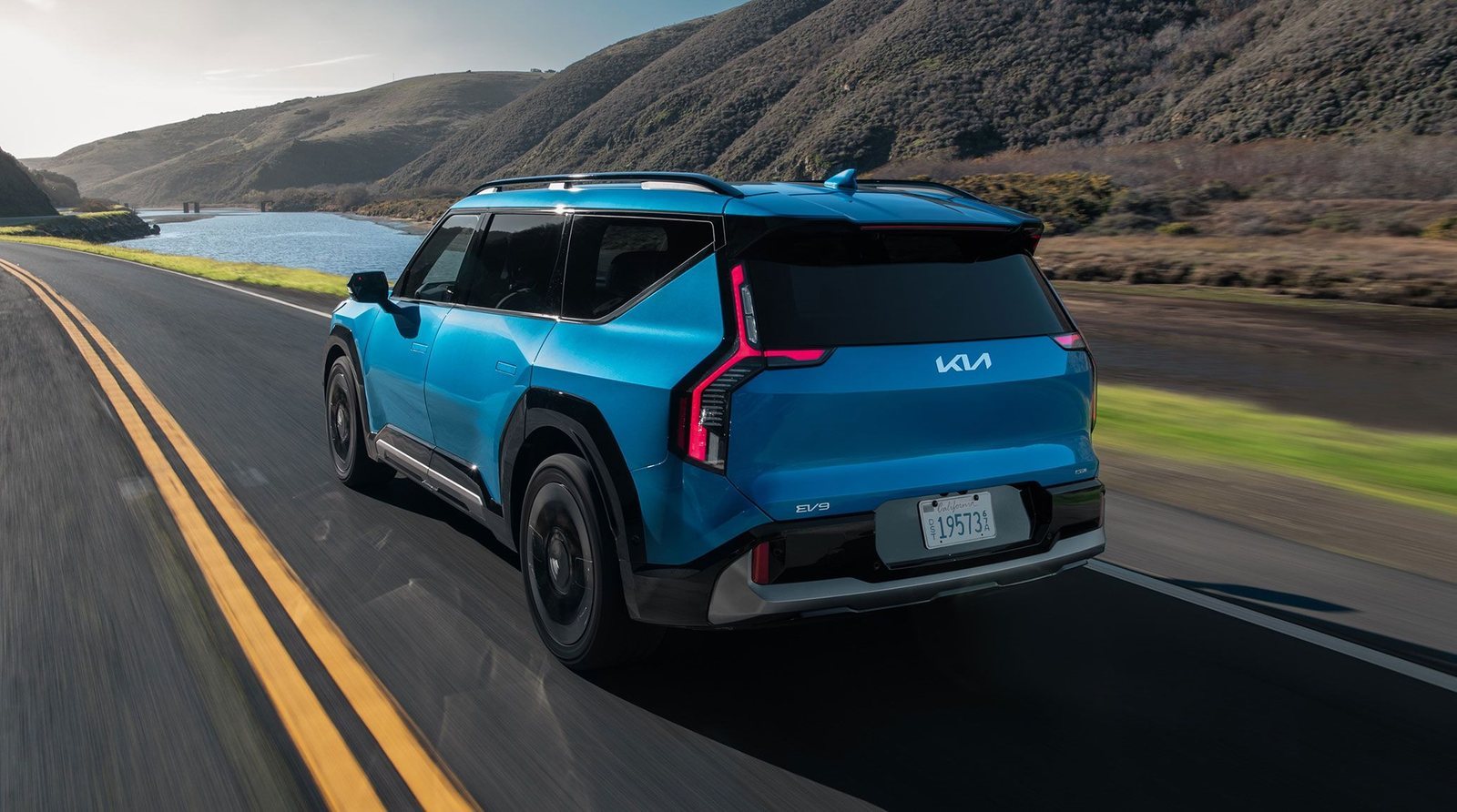 2026 Kia EV9 in blue driving on a lakeside highway