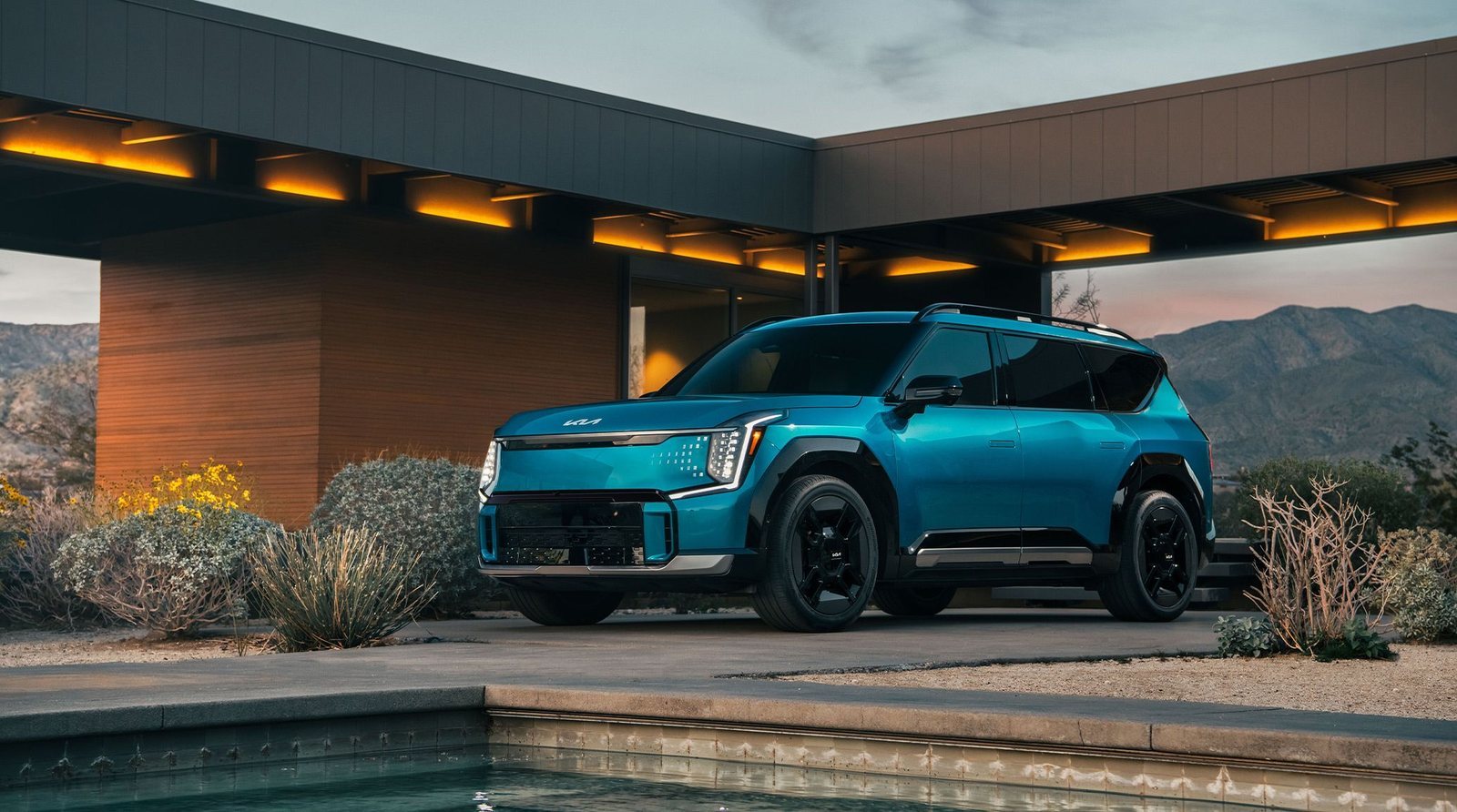 2026 Kia EV9 in teal parked outside a modern mountain home