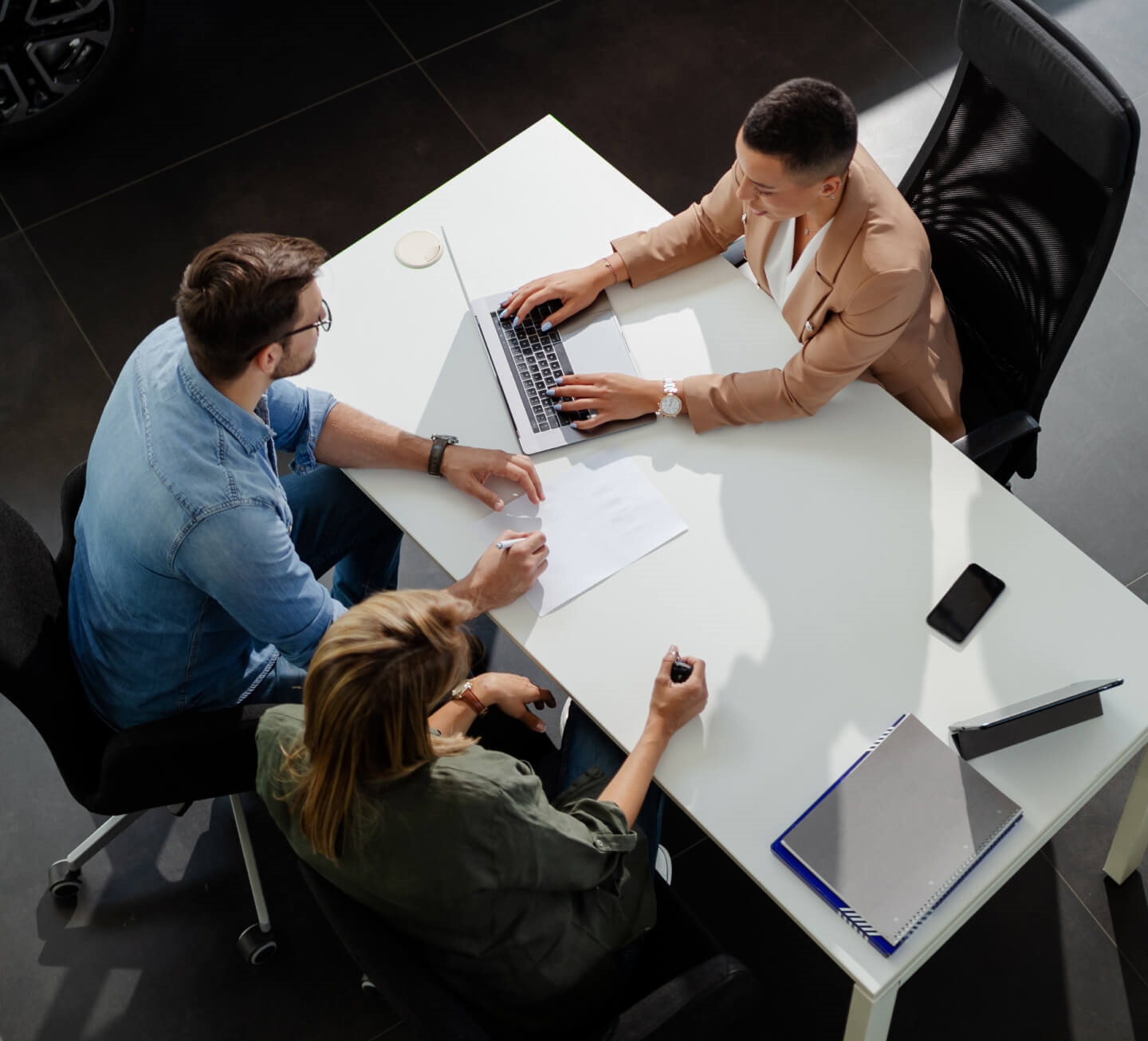 Overhead shot of a sales representative assisting customers at a desk inside a sunlit dealership.