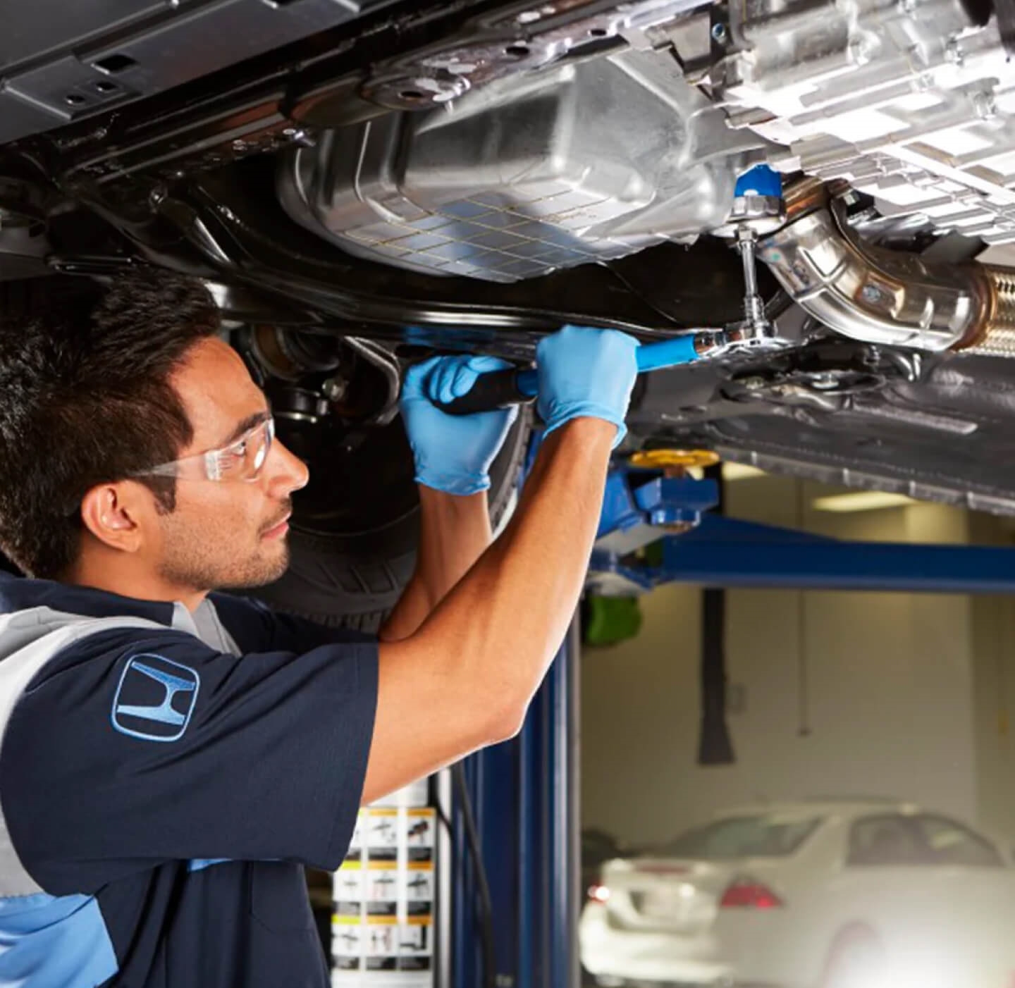 A Honda Certified Technician cranks a ratchet wrench under a lifted Honda vehicle.
