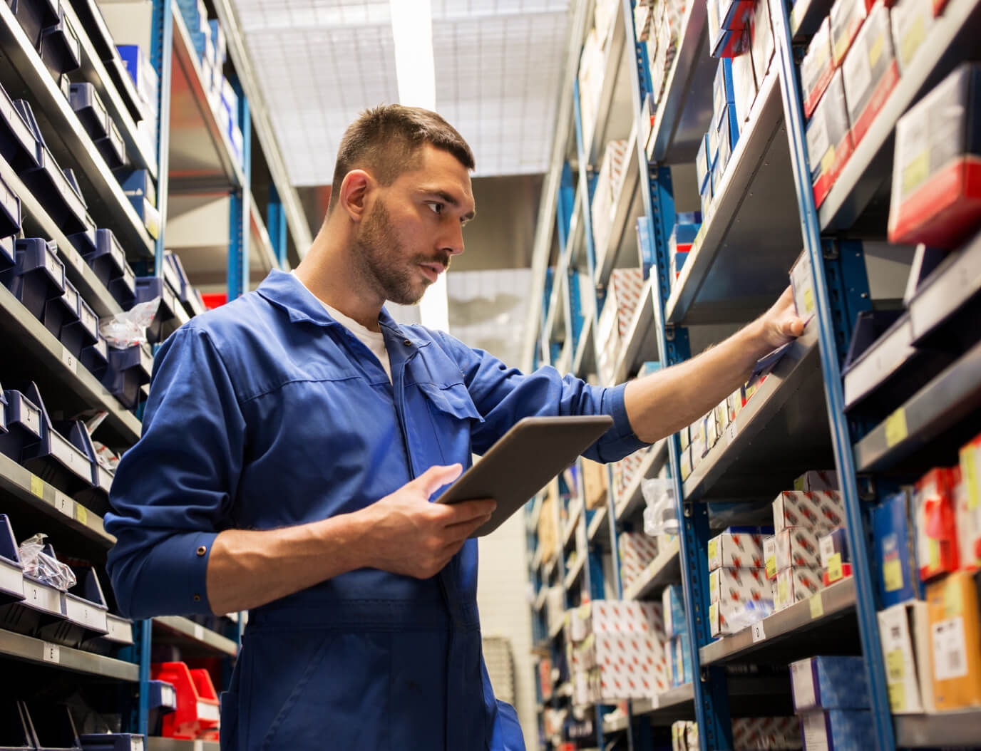 A service technician holding a clipboard grabs an auto part from a shelf.